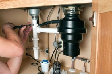 Plumber repairing a garbage disposal beneath a kitchen sink in Vero Beach