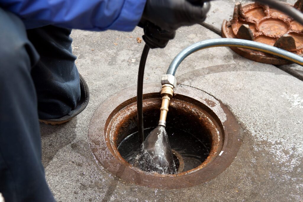 Plumber hydro jetting a sewer line through a manhole in Vero Beach