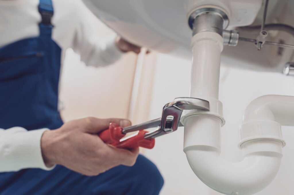 Plumber repairing a white drain pipe beneath a sink in Vero Beach