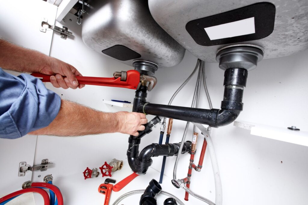 Plumber repairing drain pipes beneath a kitchen sink in Vero Beach